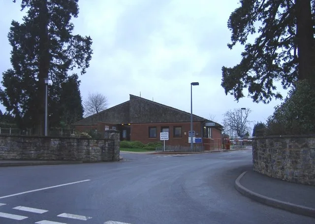 The entrance to Leyhill prison, with a low brick building beyond a driveway and stone walls.